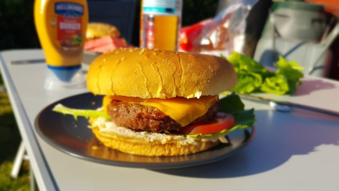 Ein selbstgegrillter Cheeseburger liegt auf einem Teller. Das Licht der Abendsonne und der passende Filter geben ihm eine Optik wie aus einem Werbeprospekt.