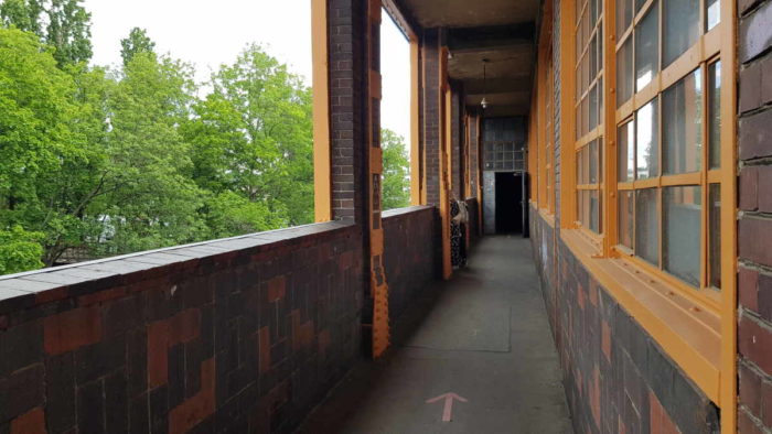 Einer der Außenrundgänge um das Glashaus. Rechts im Bild ist die Wand mit mehreren Fenstern, links eine Brüstung hinter der Bäume und die Spree zu sehen sind.
