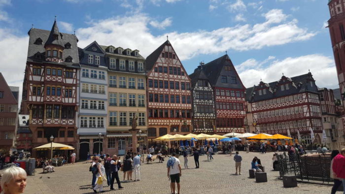 Der Römerberg mit vielen Touristen, im HIntergrund Fachwerkhäuser vor denen die Sonnenschirme von Restaurants stehen.