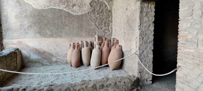 An einer Wand in einer der Ruinen von Pompei lehnen etwa 15 Amphoren an einer Wand.