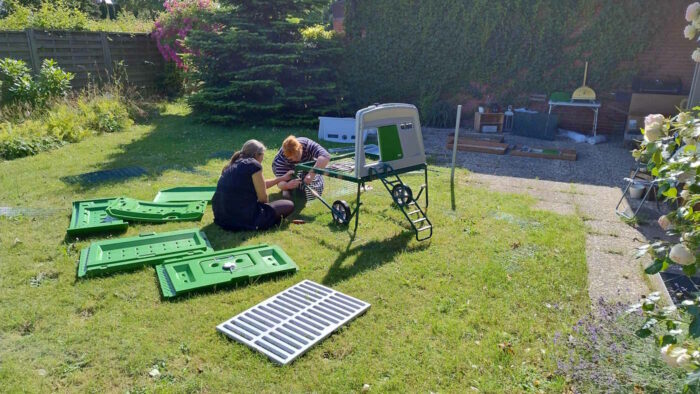 Gesche und unsere Freundin Lydia sitzen im Garten zwischen den Einzelteilen des Hühnerstalls und drehen Schrauben in das Untergestell.