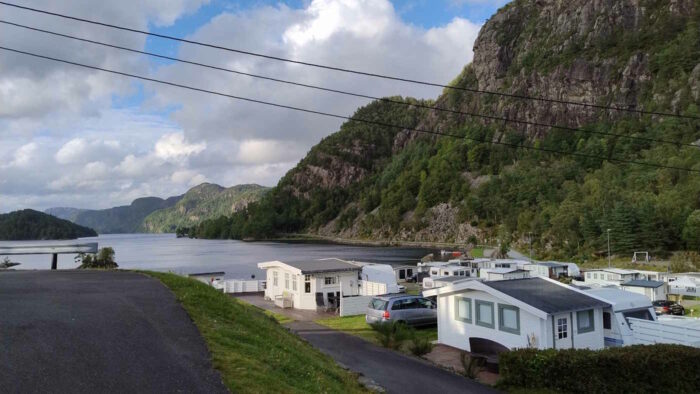 Aussicht über den Campingplatz in Flekkefjord: Man sieht im Hintergrund Felsen und den Fjord, davor sind weiß gestrichene Hütten der Dauercamper zu sehen.