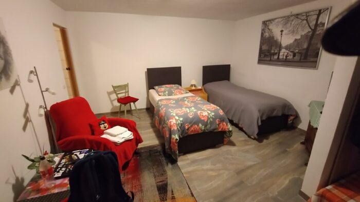 Das Bild zeigt das Wohn- und Schlafzimmer meiner Ferienwohnung. Es sind zwei getrennt voneinander stehende Einzelbetten zu sehen, außerdem verschiedene Sitzgelegeheiten. An der Wand hängt ein Bid.