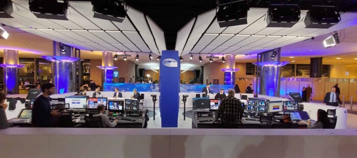 Durch eine blaue Wand getrennt sind zwei identische Studios zu sehen, die so genannten Voxboxen. Im Vordergrund jeweils die Bildregie, dahinter sitzen an Tischen mehrere Menschen und zeichnen Fernsehsendungen auf. Im Hintergrund ist der Flur zum Plenarsaal zu erkennen.
