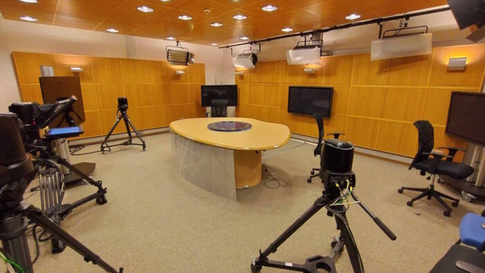 In einem holvertäfelten Raum steht ein Tisch, an dem bis zu vier Menschen Platz finden. Drei Kameras sind im Raum positioniert, eine davon hat einen Teleprompter. Hinter dem Tisch stehen drei Monitore, an der Decke hängt TV-Beleuchtung.