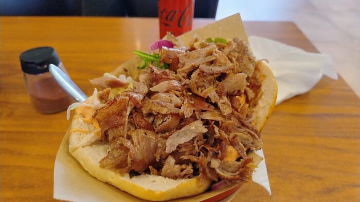 Ein appetitlicher Döner steht in einer Müslischale auf einem Tisch. Unter dem Döner ragt aus der Schale der Stiehl einer Gabel hervor.